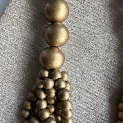 Tassel decorativo com bolas douradas metálicas e textura fosca sobre tecido cinza claro