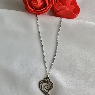 Colar prateado com pendente em forma de coração e padrões espirais sobre fundo branco e flores vermelhas.