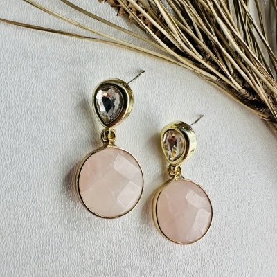 Brincos de metal dourado com pedras castanhas e rosa, com decoração de ramos secos ao lado.