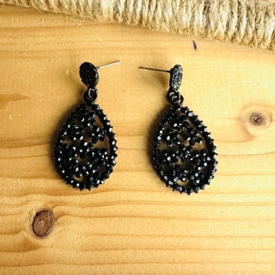Brincos pretos em forma de gota com pedras brilhantes sobre madeira.