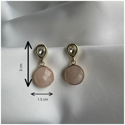 Brincos dourados com pedras transparentes e rosa claro sobre tecido branco.