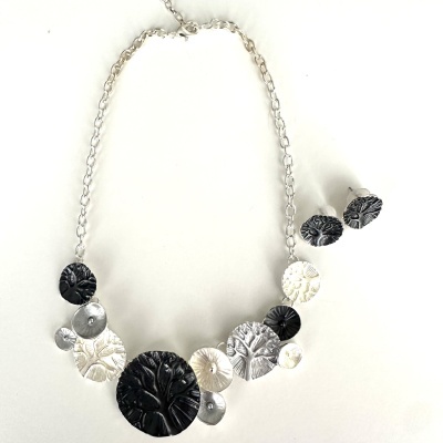 Conjunto de colar e brincos prata e preto com círculos texturizados e padrão de árvore
