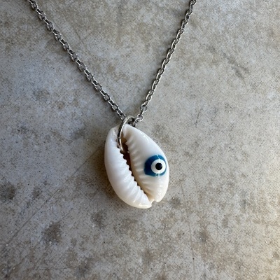 Colar com pendente de concha branca e olho azul numa superfície cinzenta