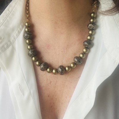 Colar com bolas douradas e esferas prateadas texturizadas, usado com camisa branca.