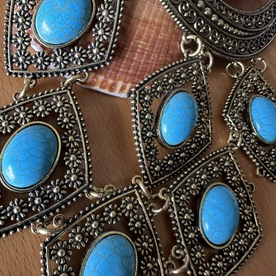 Colar dourado com pedras azuis e motivos florais, sobre superfície de madeira com concha