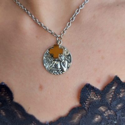 Colar prateado com medalha redonda e cruz dourada, detalhe de anjo e renda preta visível