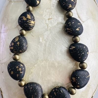 Colar com contas pretas com manchas douradas e esferas metálicas douradas sobre prato cerâmico claro