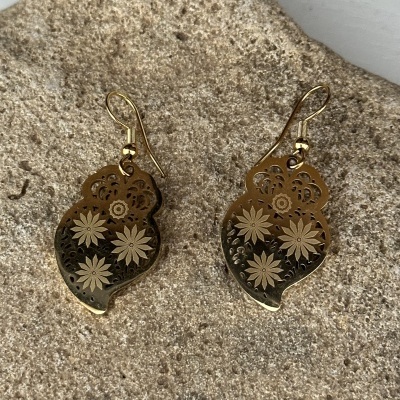 Brincos dourados com padrão floral sobre pedra texturada