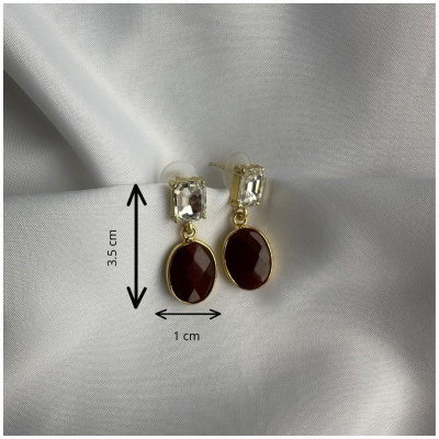 Brincos pendentes com pedra vermelha e pedra transparente sobre tecido branco