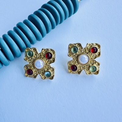 Brincos dourados com pedras coloridas ao lado de conta azul