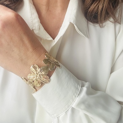 Pulseira dourada com flores grandes numa pessoa de camisa branca