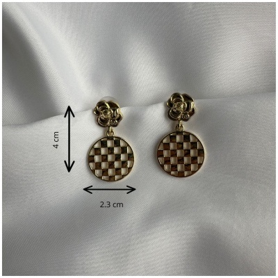 Brincos dourados com padrão quadriculado pendurados sobre tecido branco.