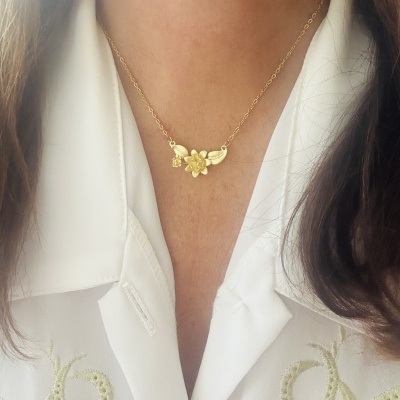Colar dourado com pendente floral usado sobre camisa branca bordada