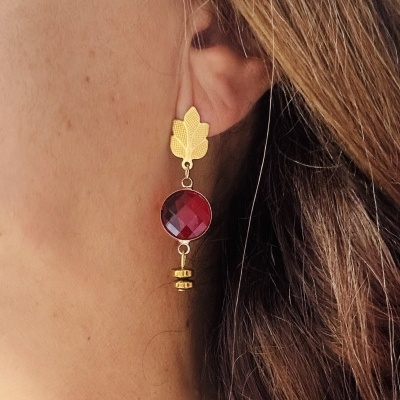 Brinco dourado com pedra vermelha e detalhe de folha na orelha