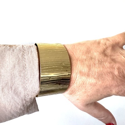 Pulseira larga dourada com textura riscada num pulso