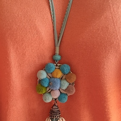 Colar comprido com pompons coloridos e moedas pendurado sobre camisola laranja