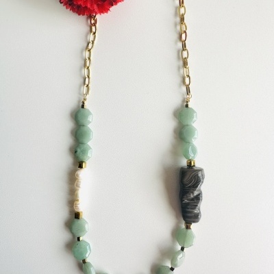 Colar de contas verdes e pretas com corrente dourada e flor vermelha ao fundo