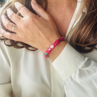 Pulseira vermelha com padrão floral usada no pulso de uma mulher com camisa branca