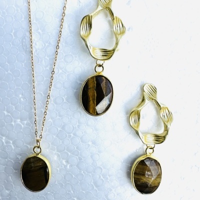Colar e brincos dourados com pedras ovais castanhas sobre fundo branco.