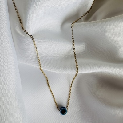 Colar dourado com pendente olho azul sobre tecido branco.