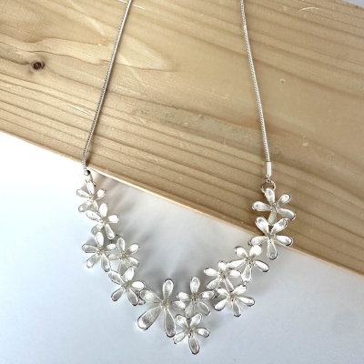 Colar prateado com flores estilizadas em cima de madeira clara