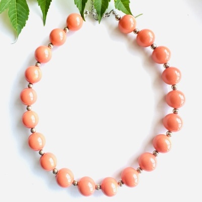 Colar de contas salmão e metálicas sobre fundo branco com folhas verdes