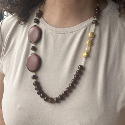 Colar com contas castanhas, ovais de madeira clara, douradas e brancas usado em t-shirt bege