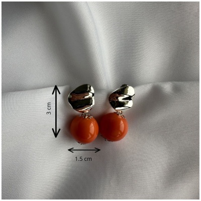 Brincos com base metálica prateada e esfera laranja pendurada sobre tecido branco.