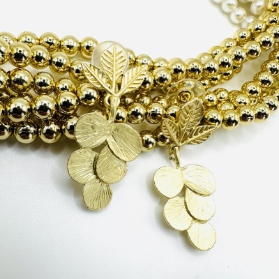 Brincos dourados com pendente de folhas sobre colares de pérolas e esferas douradas