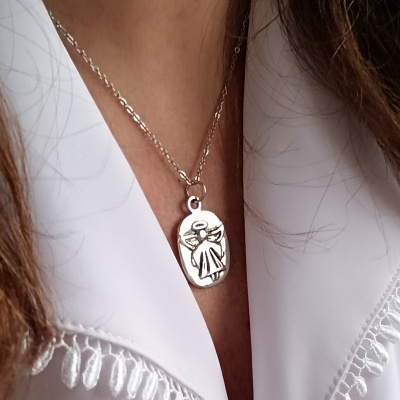 Colar prateado com pendente oval e gravação de anjo sobre tecido branco com bordado