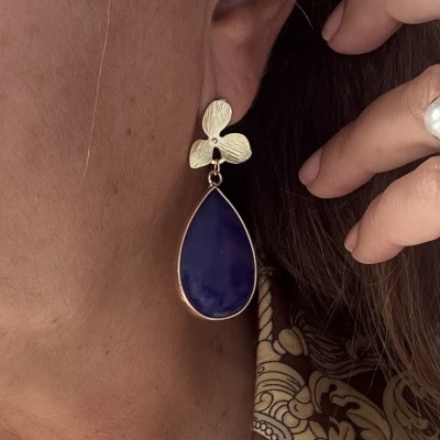 Brinco dourado com gota azul pendente, visto de perto no ouvido de uma pessoa