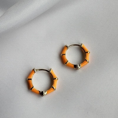 Brincos argola dourados com segmentos laranja sobre tecido branco