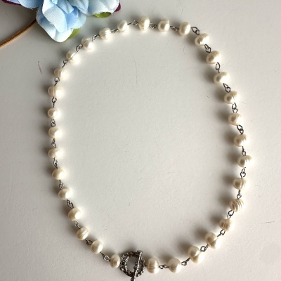 Colar de pérolas brancas com fecho prateado e flor azul ao lado