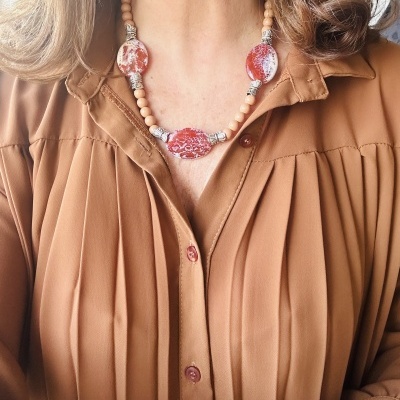 Colar com contas vermelhas e madeira claro sobre camisa castanha com pregas
