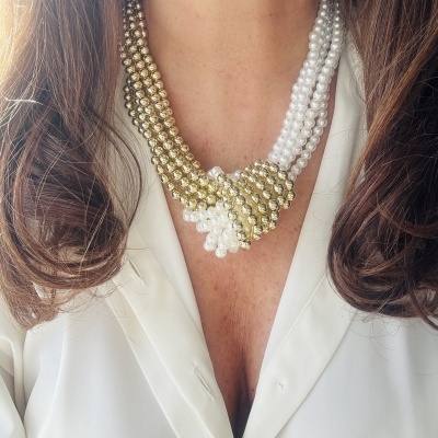 Colar de pérolas douradas e brancas entrelaçadas ao pescoço com camisa branca