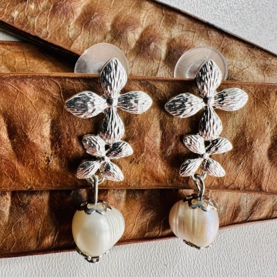 Brincos prateados com flores e pérolas sobre couro castanho