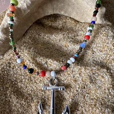Colar com contas coloridas e pendente de âncora prateada sobre areia