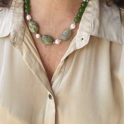 Colar com pedras verdes, pérolas brancas e detalhes metálicos em pescoço com camisa bege