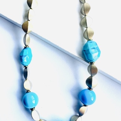 Colar com contas azuis e peças metálicas douradas sobre fundo branco.