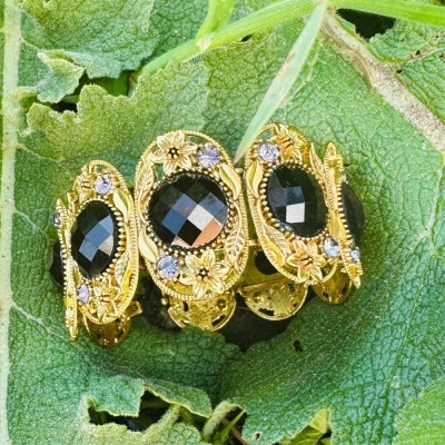 Anel dourado com pedras pretas sobre folha verde