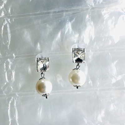 Brincos com pedras quadradas transparentes e pérolas brancas sobre fundo plástico