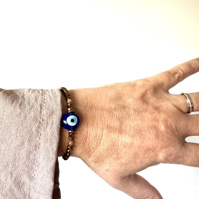 Pulseira com conta azul olho turco no pulso de uma pessoa com camisa bege.