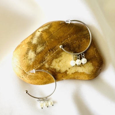 Brincos de aro prateado com pérolas sobre pedra castanha