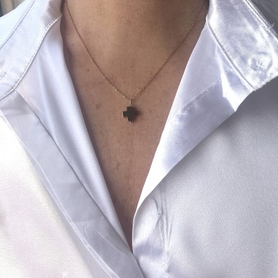 Colar dourado com pendente em cruz preta com camisa branca acetinada