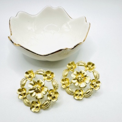 Tigela branca de cerâmica com bordas douradas e brincos dourados em forma de flores