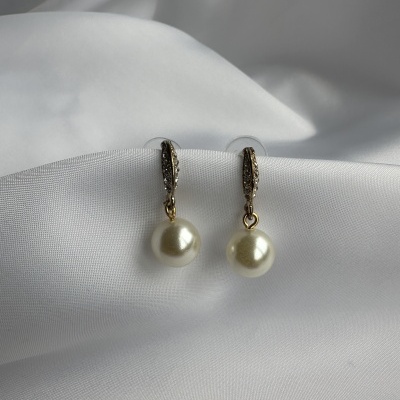 Brincos pendentes com pérolas e gancho dourado sobre tecido branco