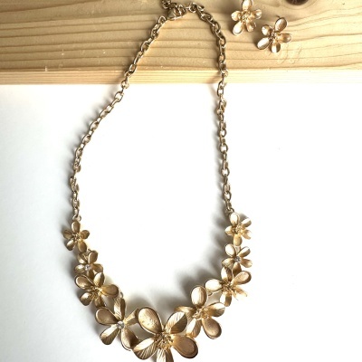 Colar e brincos dourados com design floral sobre fundo branco e madeira.