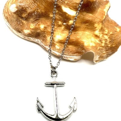 Colar prateado com pendente de âncora sobre concha bege com manchas