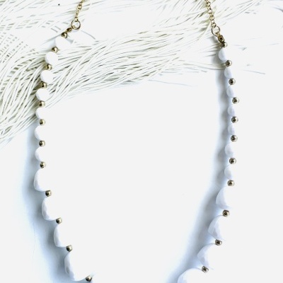 Colar com pedras brancas e detalhes dourados sobre tecido branco texturizado