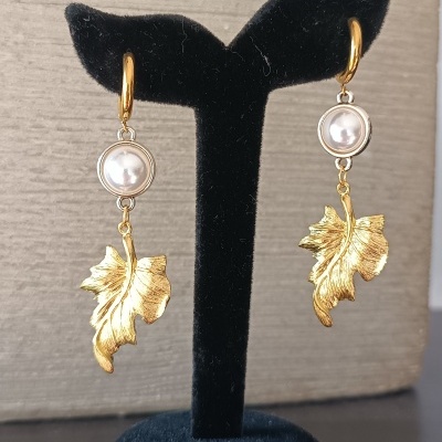 brincos dourados com pérolas e folhas penduradas num suporte preto